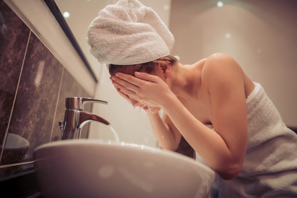 Young woman washing her face in bathroom.