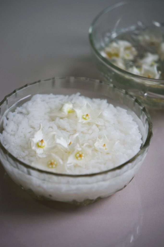 A Bowl Containing Rice Soaked in Water and Garnished with White Petals