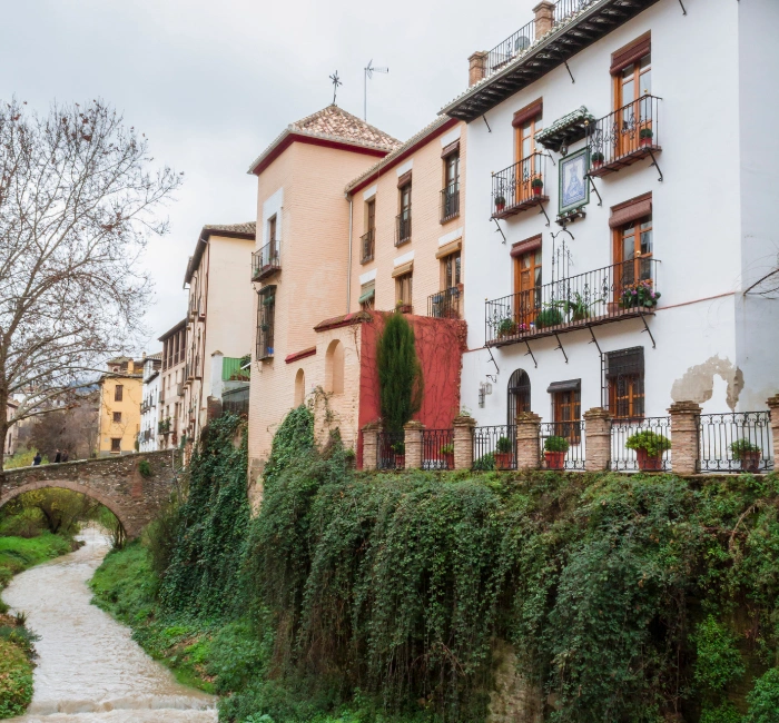 Charming street in Granada, Spain, featuring traditional Spanish architecture and lush greenery along a serene canal.