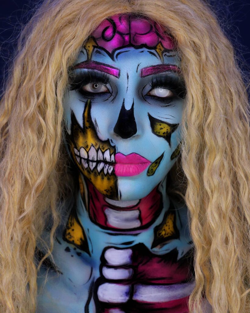 A person with comic-style zombie makeup in blue, pink, and yellow, featuring an exposed brain, cracked skull, decayed teeth, and long blonde wavy hair.