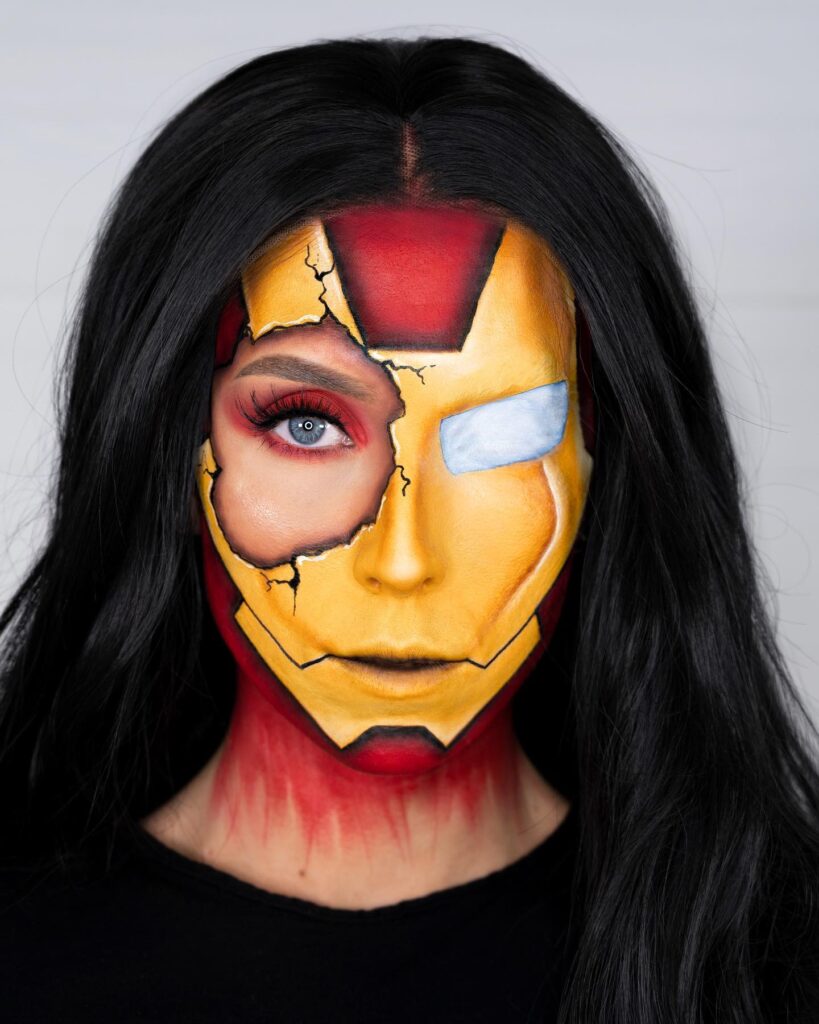 A person with half of their face painted as Iron Man, featuring bold red and yellow metallic details with cracks and a dramatic exposed eye.