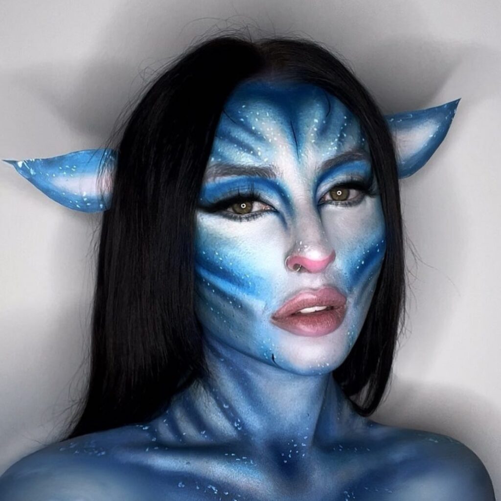 A person with Avatar-inspired blue face and body paint, white dots, pink nose, and elongated ears, resembling a Na'vi character.