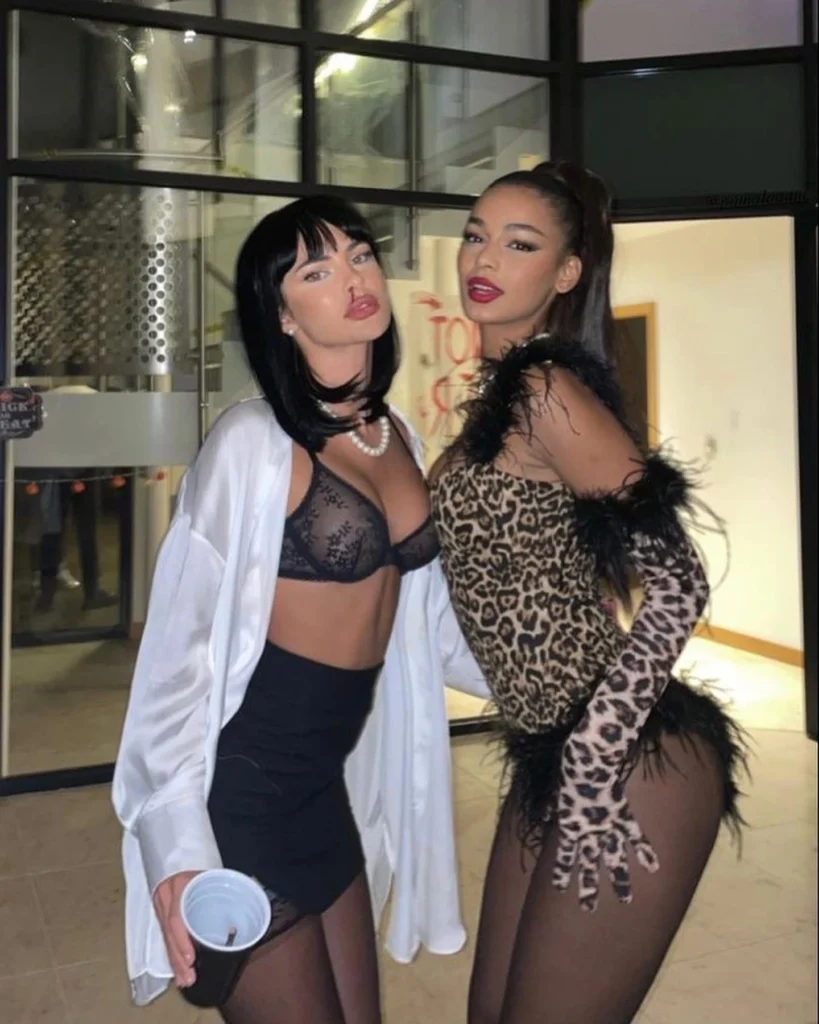 Two women dressed in chic party outfits, one wearing a black lace bralette with a mini skirt and satin shirt, the other in a leopard-print bodysuit with feather trim.