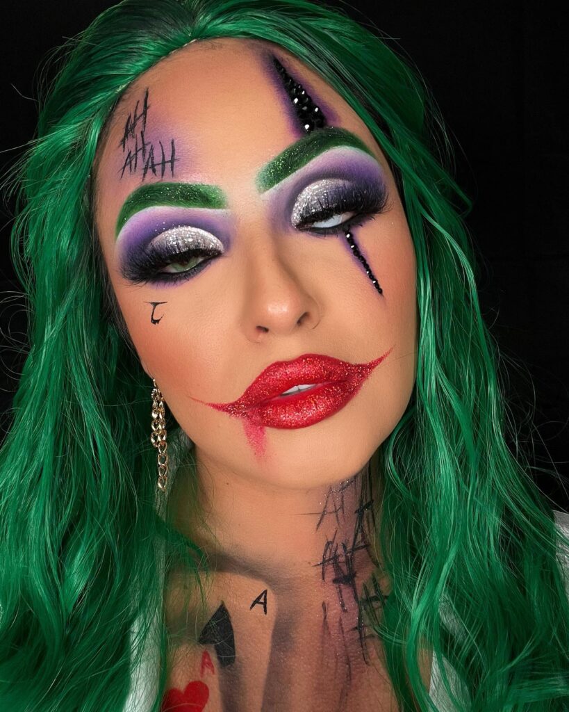 Woman with green hair, bold green brows, purple and silver eyeshadow, and exaggerated red glitter lips styled in a Joker-inspired look.