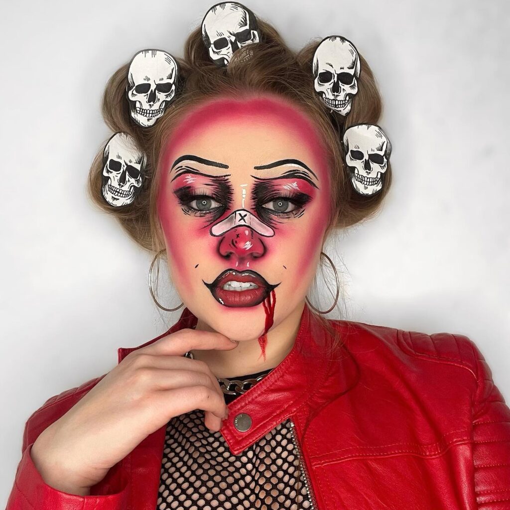 A person wearing bold punk clown makeup, featuring a pink nose, exaggerated blush, blood drips, and skull hair rollers. They are dressed in a red leather jacket, completing the edgy and eerie style.