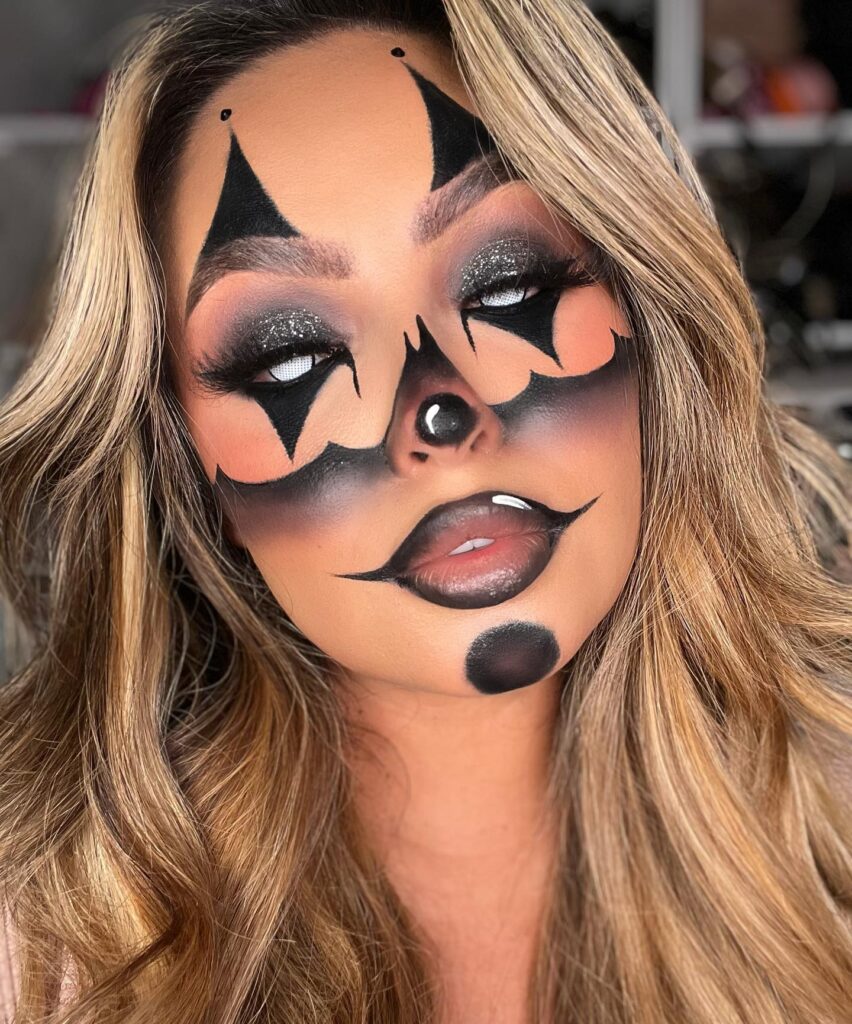 Close-up of a woman with bold black and pink clown makeup, featuring dramatic black shapes around the eyes and lips.