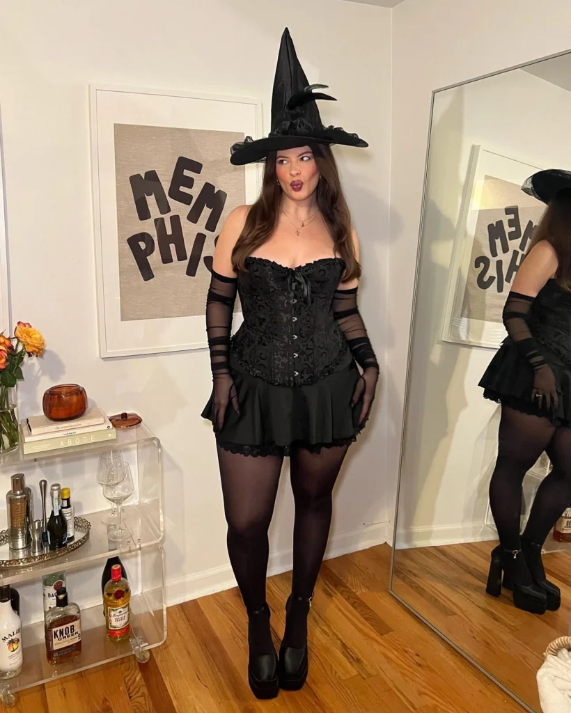 Woman dressed in a chic witch costume with a black corset and matching hat.