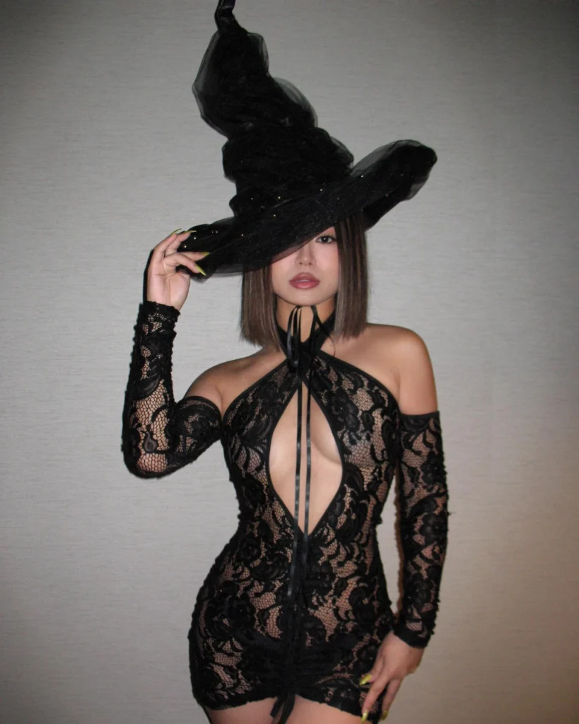 Woman in a lace witch costume with a large black hat, showcasing a dramatic and seductive Halloween style.