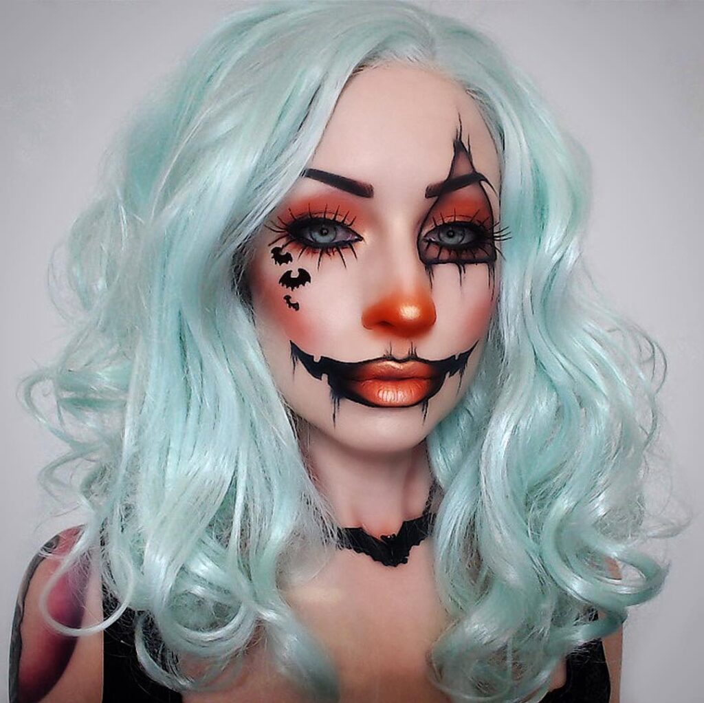 A person with a horror clown-inspired makeup look featuring orange nose and lips, black smudges around the eyes, and wavy light blue hair.