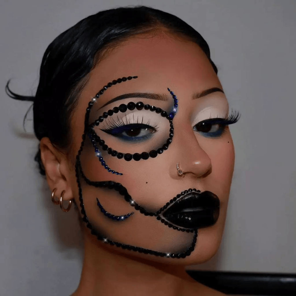 Close-up of a woman with creative black bead makeup design outlining her face, accented with dramatic white eyeshadow, black lipstick, and long lashes.