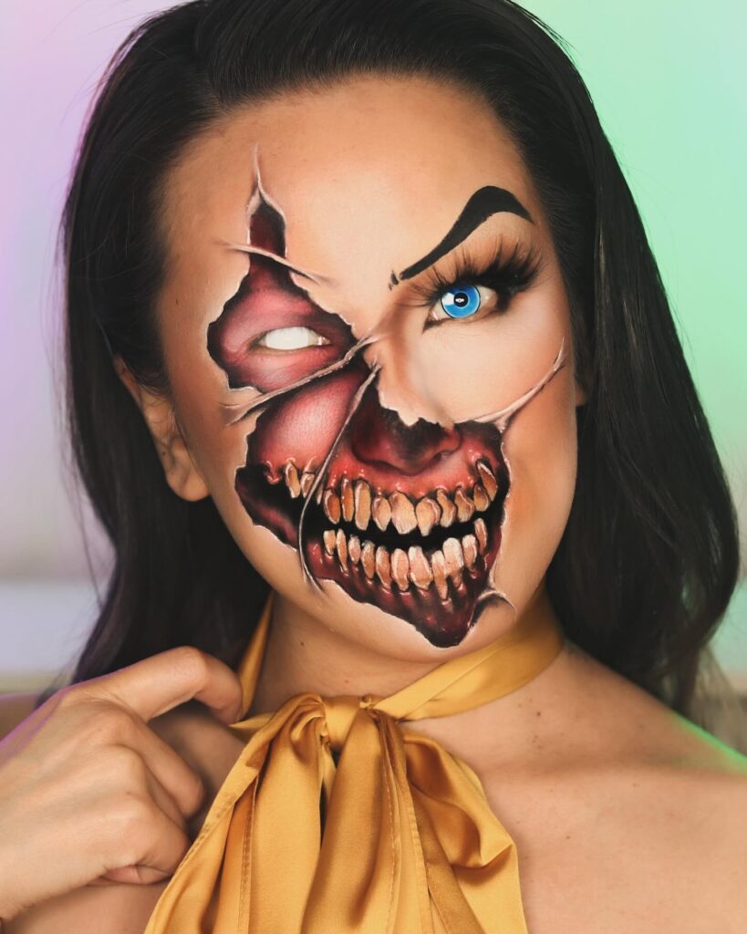 A person with a split-face makeup design, featuring one side as a normal face and the other as a monster with decayed teeth and a blue eye.