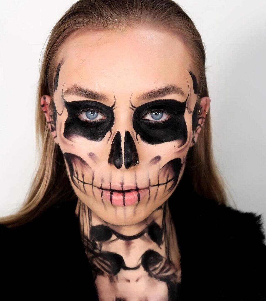 Close-up of a person wearing black and white skull makeup, emphasizing dark eye sockets and sharp cheekbone details.