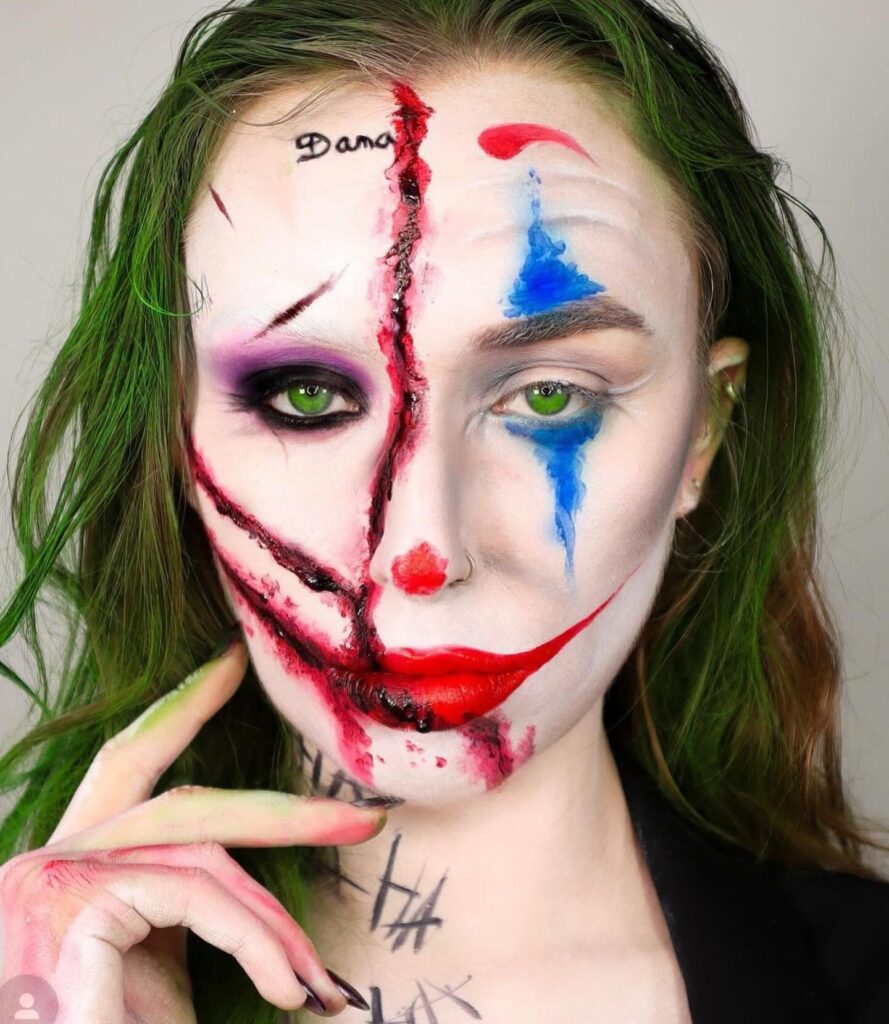 Person wearing Joker-inspired Halloween makeup with dual designs featuring clown elements on one side and a scarred, bloodied smile on the other, complemented by green hair and striking green eyes.