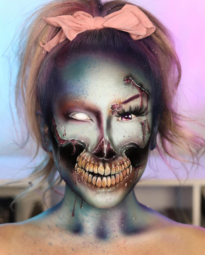 Person wearing glowing undead skull Halloween makeup with decayed teeth, glowing teal and purple skin, and white contacts, adorned with a pink bow for a creepy yet glamorous look.