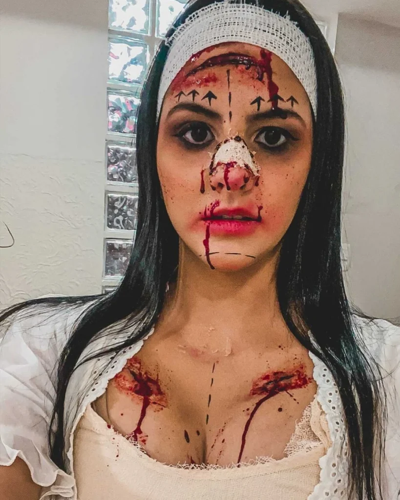 Close-up of a woman with Halloween makeup resembling a botched surgery, featuring bloodied bandages, surgical markings on her face, and realistic wounds on her chest and face, creating a disturbing and eerie appearance.