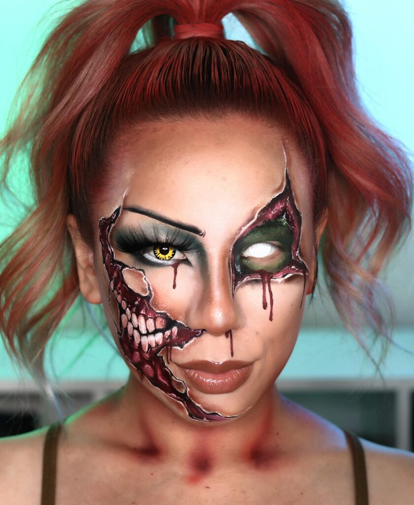 Person wearing glam zombie Halloween makeup with torn skin, exposed teeth, smoky green eyeshadow, white contact lens, and a high ponytail for a glamorous yet creepy look.