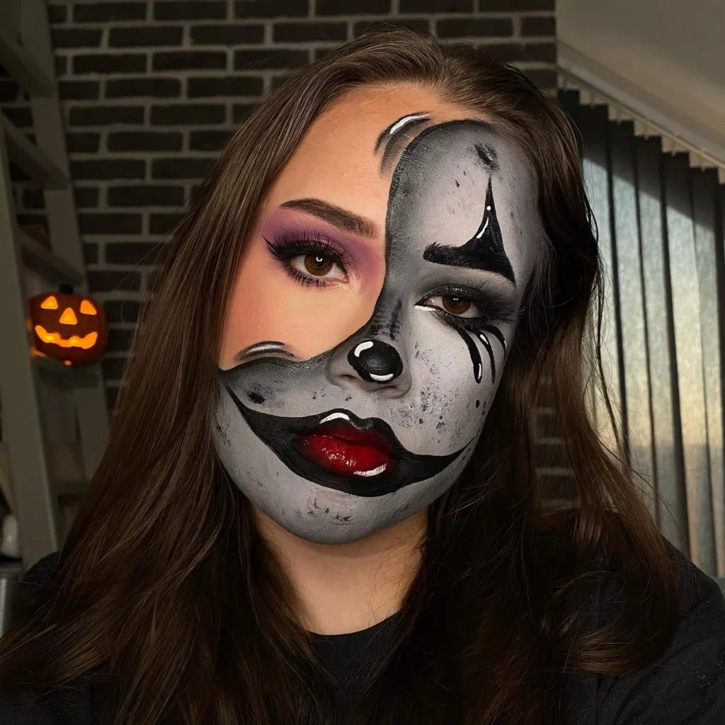 Close-up of a woman with a dual Halloween makeup look: one side features glamorous makeup with purple eyeshadow and red lips, while the other side is a black-and-white clown design with exaggerated features and dark, dramatic lines.