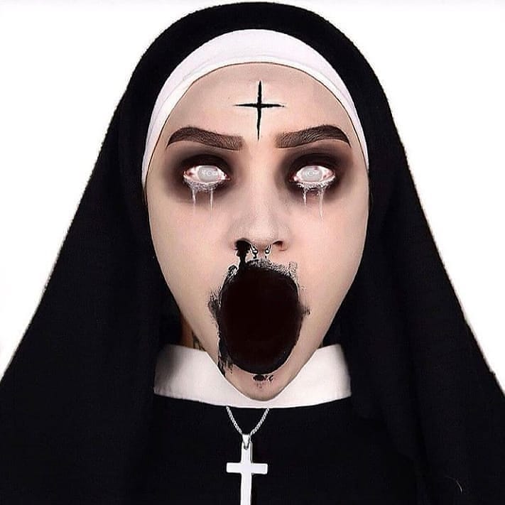 Person wearing possessed nun-inspired Halloween makeup with hollowed-out mouth, white eyes, dark eye makeup, and a cross on the forehead, dressed in a nun's habit for a frightening look.