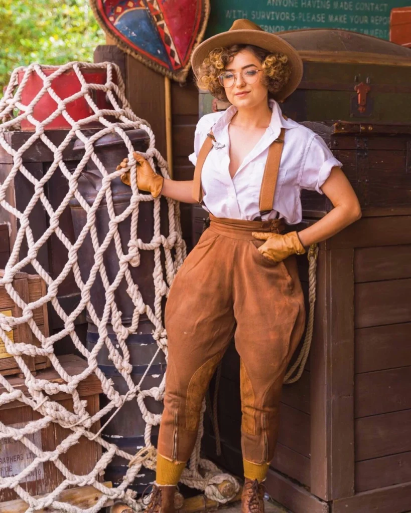 d in a vintage adventurer outfit with high-waisted brown pants, suspenders, a white shirt, wide-brimmed hat, and leather gloves.