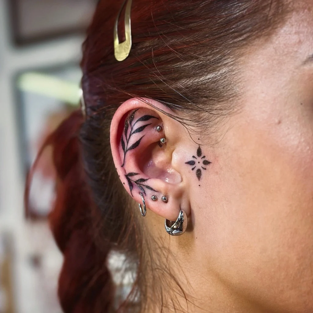 Close-up of a floral and star-shaped tattoo on a woman's ear with multiple piercings.